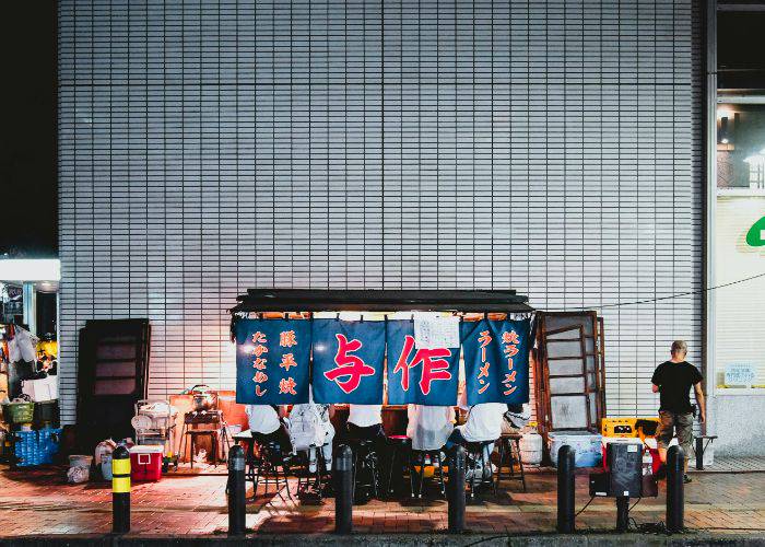 Five people hidden by the curtain of a yatai street food stall in Fukuoka.